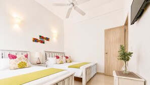Une chambre d’hôtel avec deux lits, un ventilateur de plafond, un radiateur, un téléviseur fixé au mur et une porte en bois.