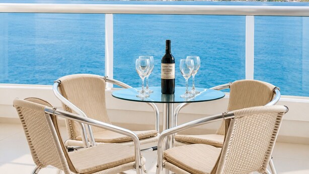 Une table avec une bouteille de vin et deux verres, placée sur un balcon donnant sur une étendue d’eau.
