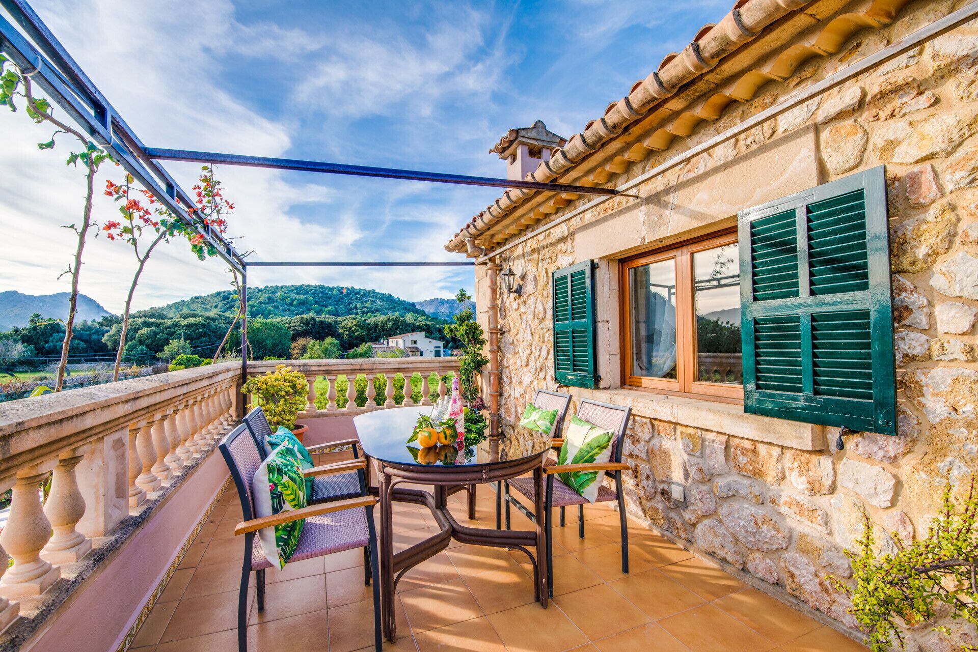 A stone building with a balcony, green shutters, and a table with chairs.