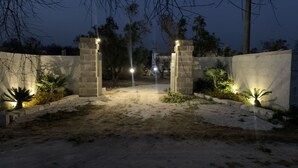 Ein verschlossener Eingangsbereich mit steinernen Säulen und beleuchteten Lichtern, der zu einem Weg führt.