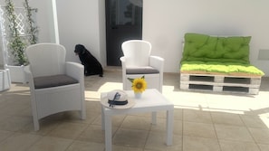 Un patio con mobiliario de mimbre, un perro y un girasol sobre una mesa.