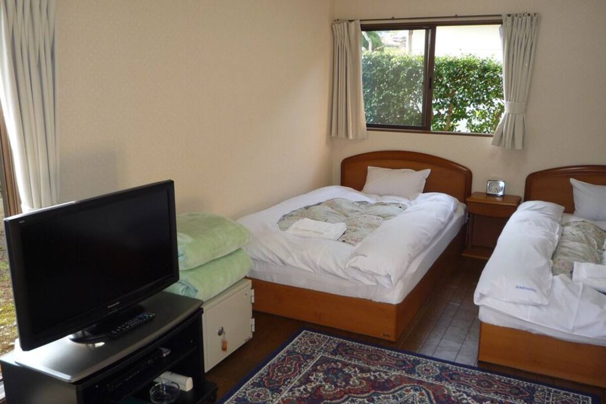 A hotel room with two beds, a television, a nightstand, and a window with curtains.
