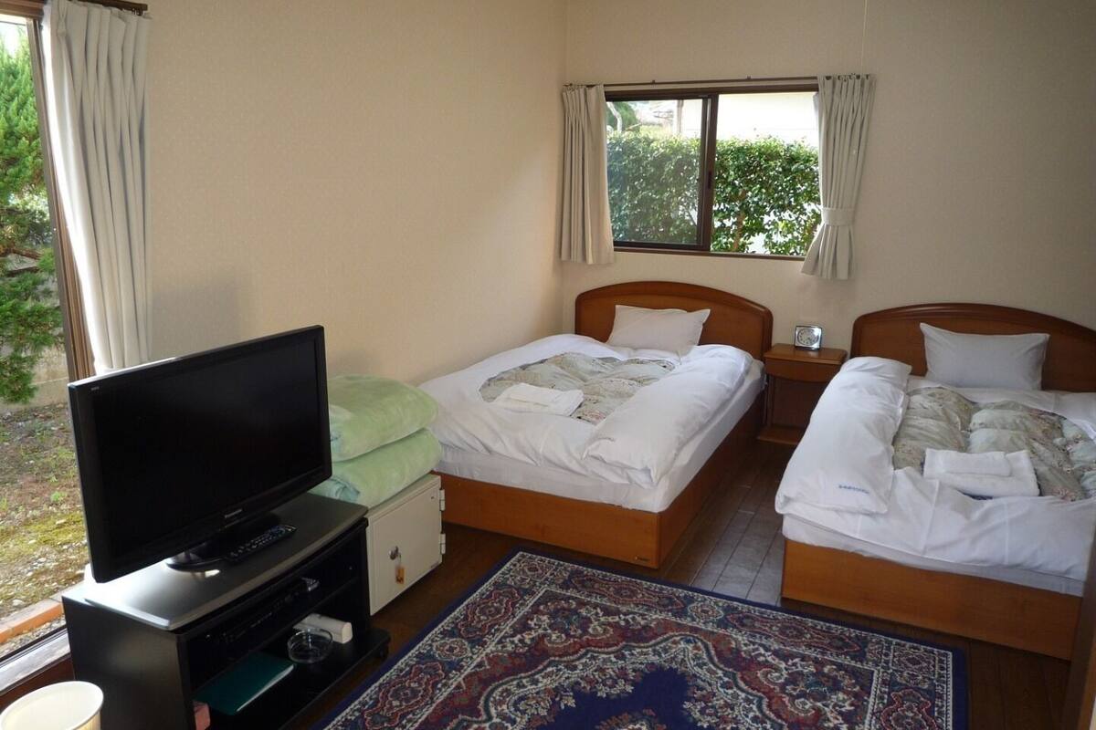 A hotel room with two beds, a TV, a small desk, and a window with curtains.