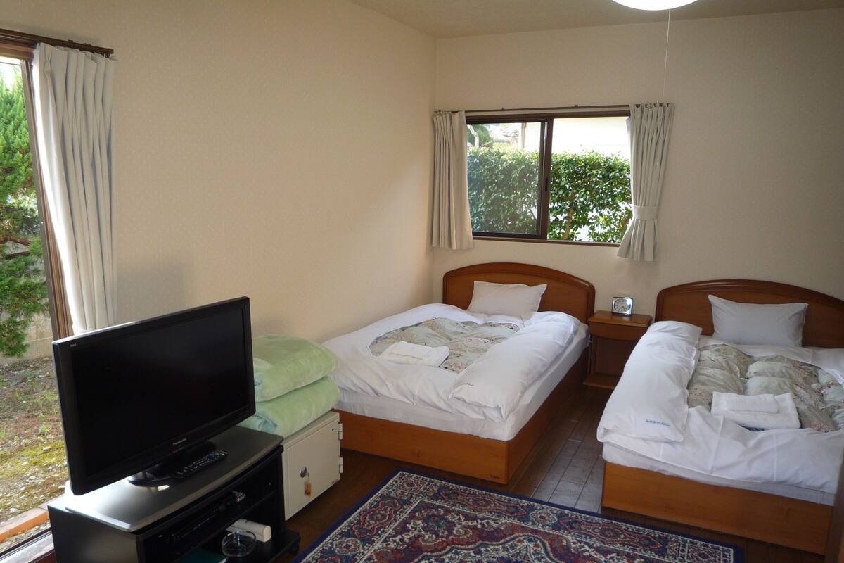 A hotel room with two beds, a television, a small table, and a window with curtains.