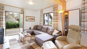 Una sala de estar acogedora con un sofá modular, una mesa de centro y un televisor. Se observa una ventana con cortinas, una lámpara y una estantería.