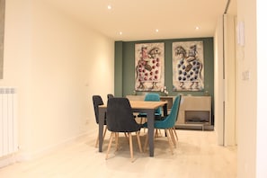 A dining area with a wooden table and chairs, a kitchen in the background, and two large abstract paintings on the wall.