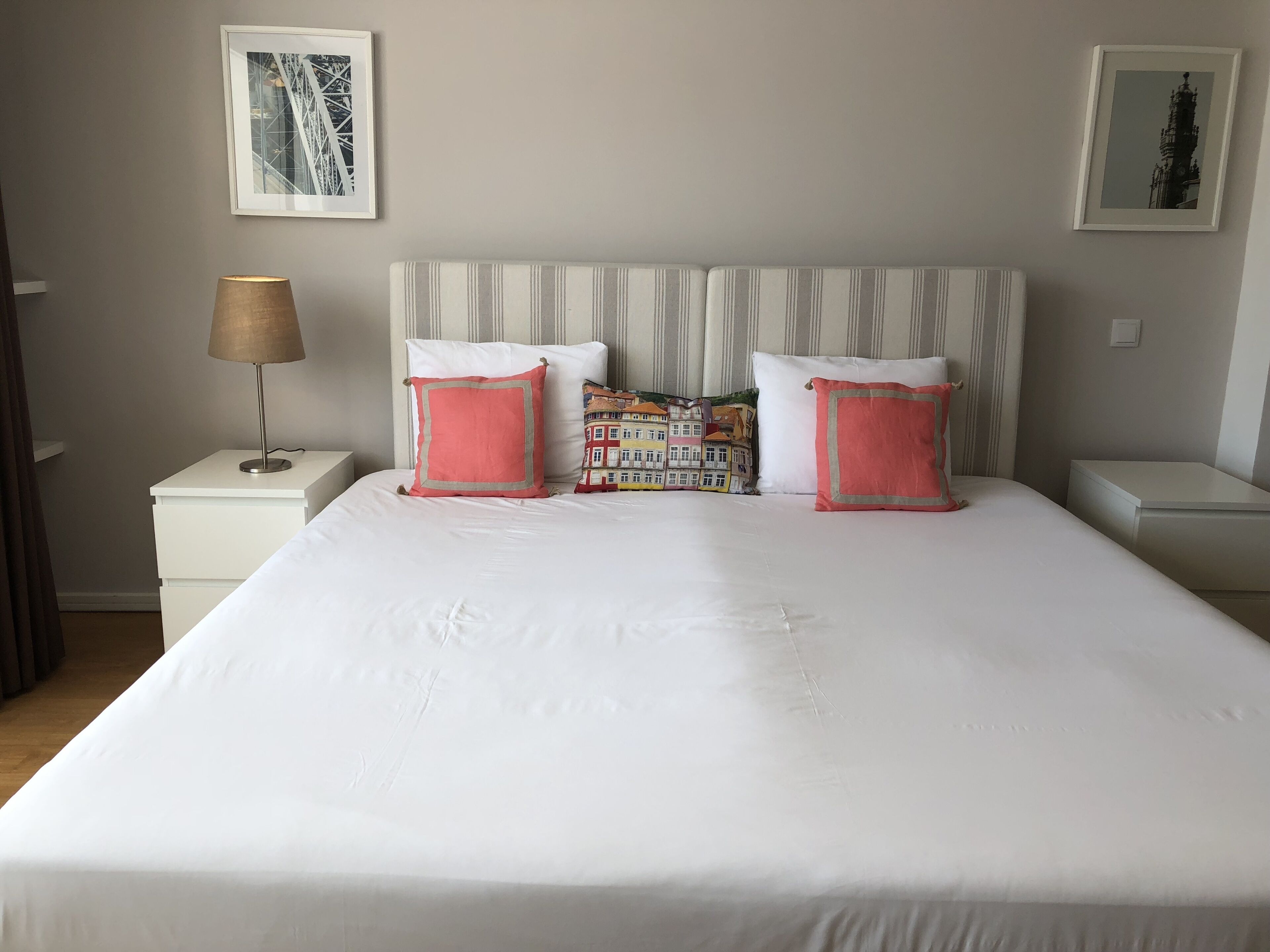 Een netjes opgemaakt bed met witte beddengoed en twee roze kussens, een gestreept hoofdeinde en een lamp op een nachtkastje.