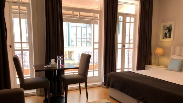 Habitación de hotel con cama, escritorio y sillas, una mesa con botellas de agua, y vistas a través de amplias ventanas.