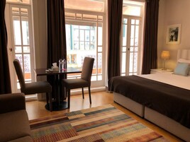 Quarto de hotel com uma cama, uma mesa com cadeiras, uma mesa com garrafas de água e vista através de grandes janelas.