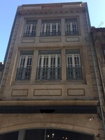 Um edifício com vários andares, grandes janelas e grades de ferro decorativas.