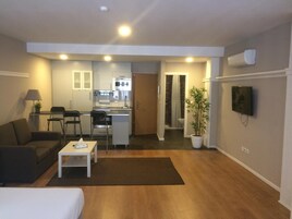 Um espaço compacto com cozinha compacta, área de refeições, espaço de estar com sofá e mesa de centro, e uma TV fixada na parede.