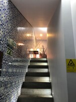 Uma escadaria com azulejos decorados em azul nas paredes, corrimão e um aviso na parede.