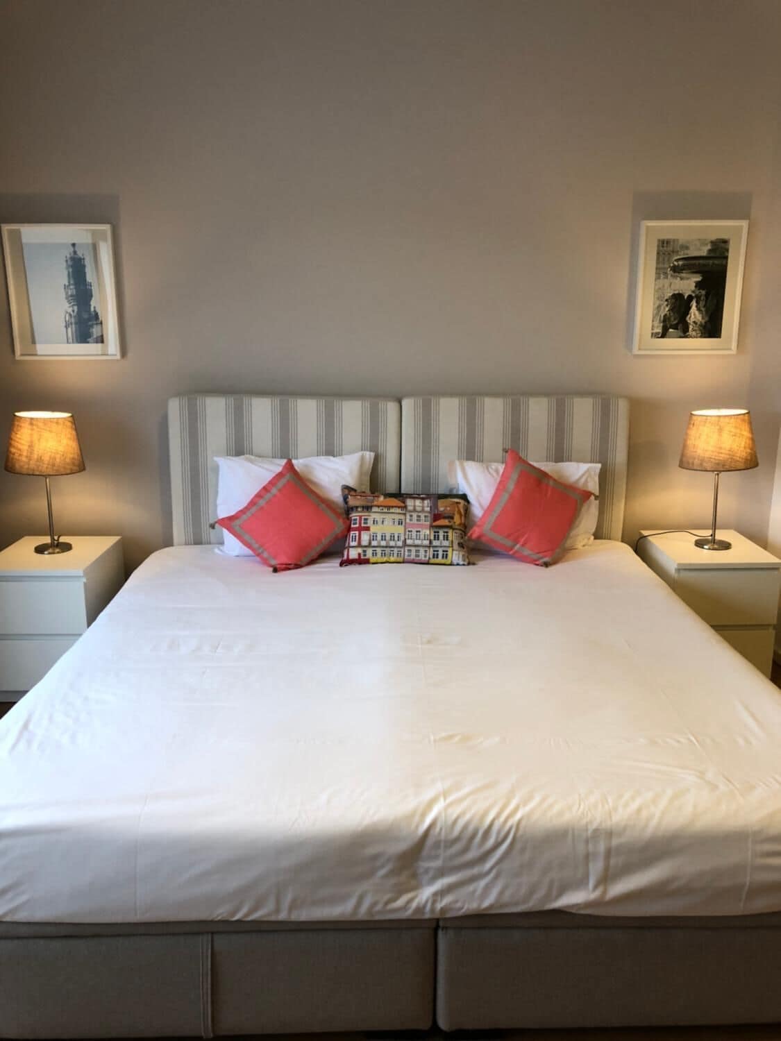 A neatly made bed with white bedding and striped headboard, flanked by two bedside lamps and a small bedside table.