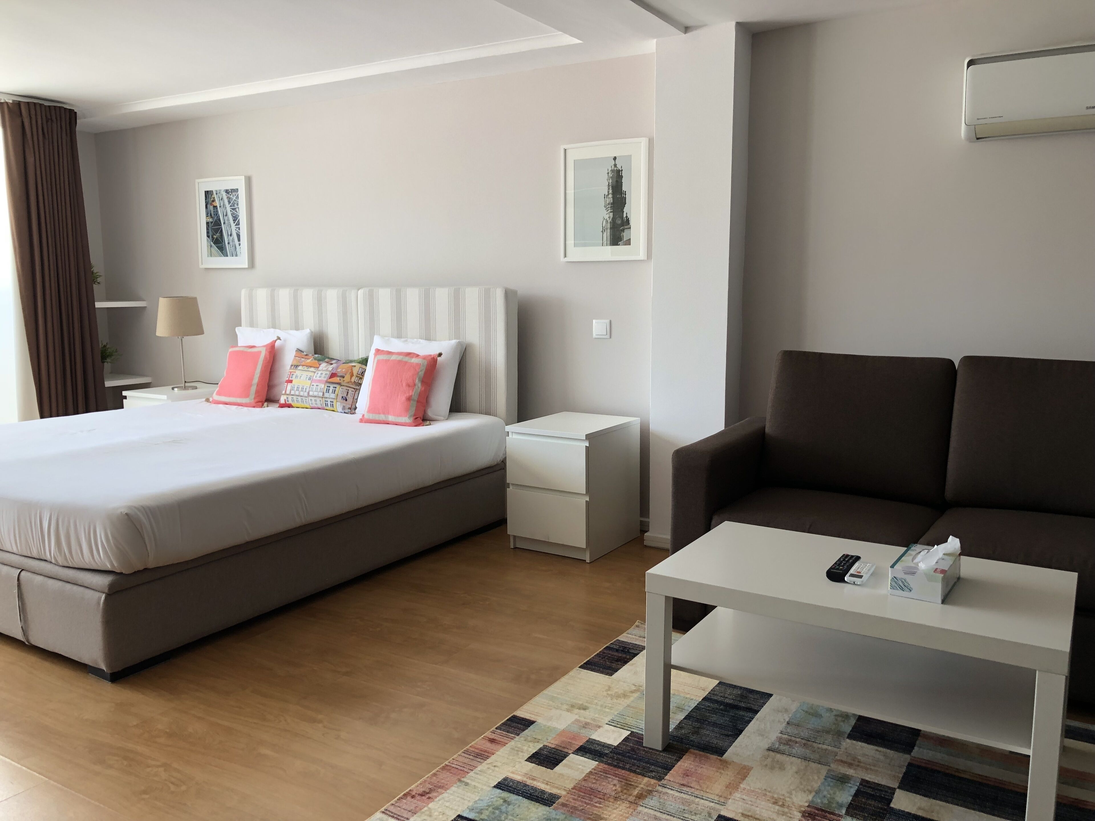 A modern hotel room with a large bed, a sofa, a small table, and a nightstand.