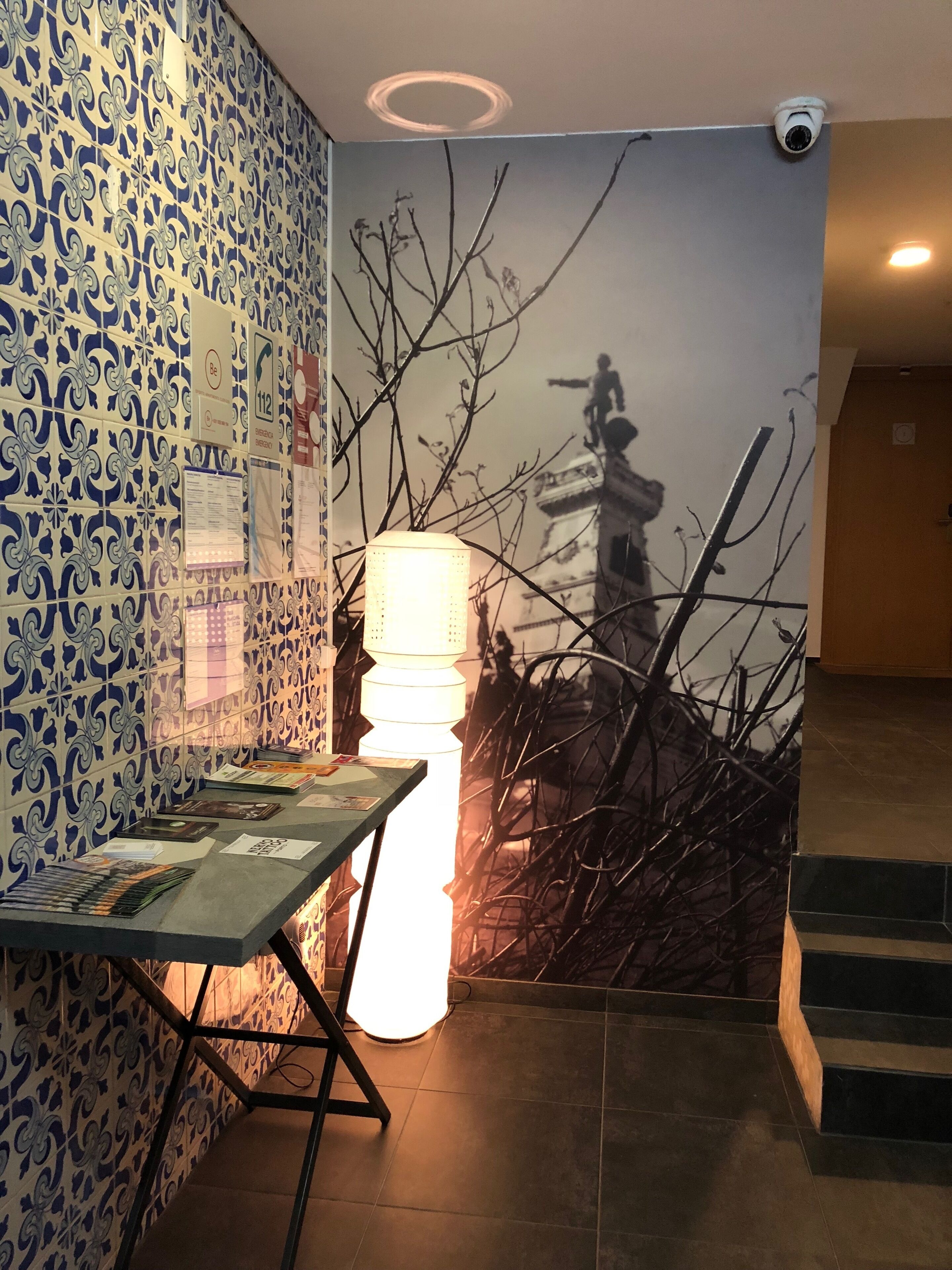 Et værelse med tapet på væggene, et bord med magasiner, en lampe og et vægmaleri af en statue.