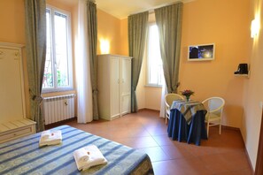 A hotel room with a bed, a table with a tablecloth, a chair, a cabinet, and a television on the wall. - Vatican Town (Rome)
