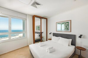 Une chambre d’hôtel avec un grand lit, une vue sur la mer, un miroir et des œuvres d’art accrochées au mur.