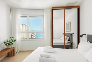 Una habitación de hotel con una cama, una mesita de noche, un espejo, una ventana con cortinas y una planta en maceta.