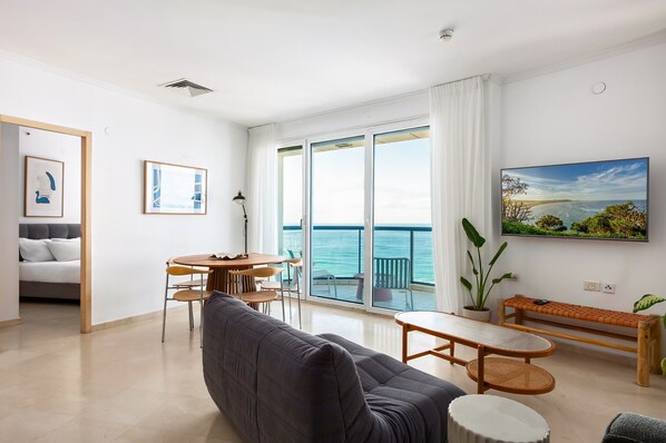 Un salon moderne avec un canapé, une table à manger et des chaises, un balcon offrant une vue sur la mer et un tableau accroché au mur.