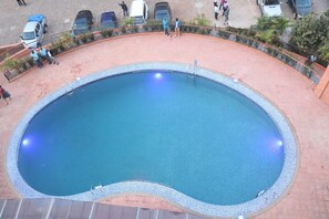 A large, oval-shaped pool with a pebble-lined edge, surrounded by a brick walkway and a metal railing. - Sainte Famille Hotel (Kigali)