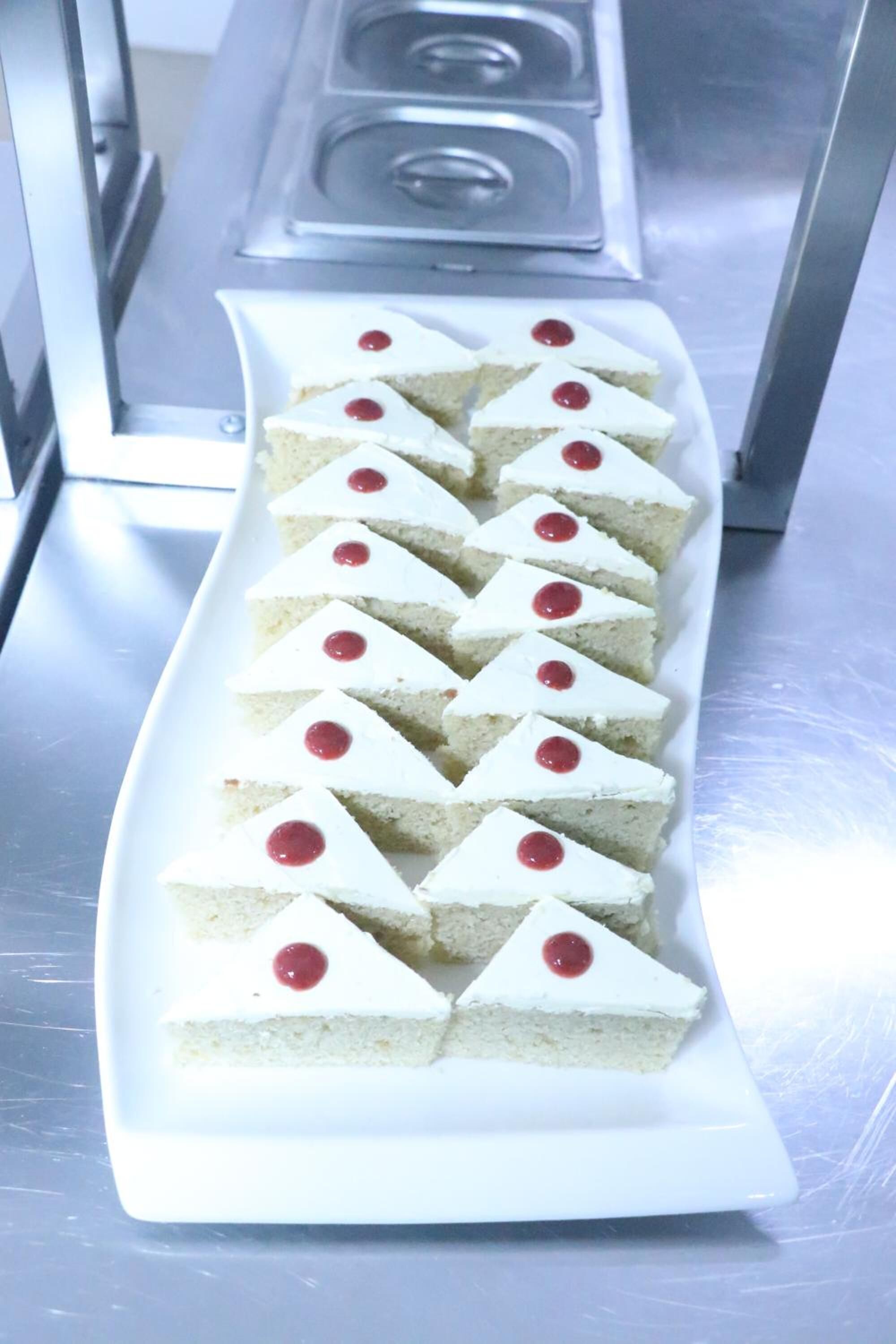 Um prato branco retangular com fatias triangulares de bolo, cada uma coberta com uma cereja.