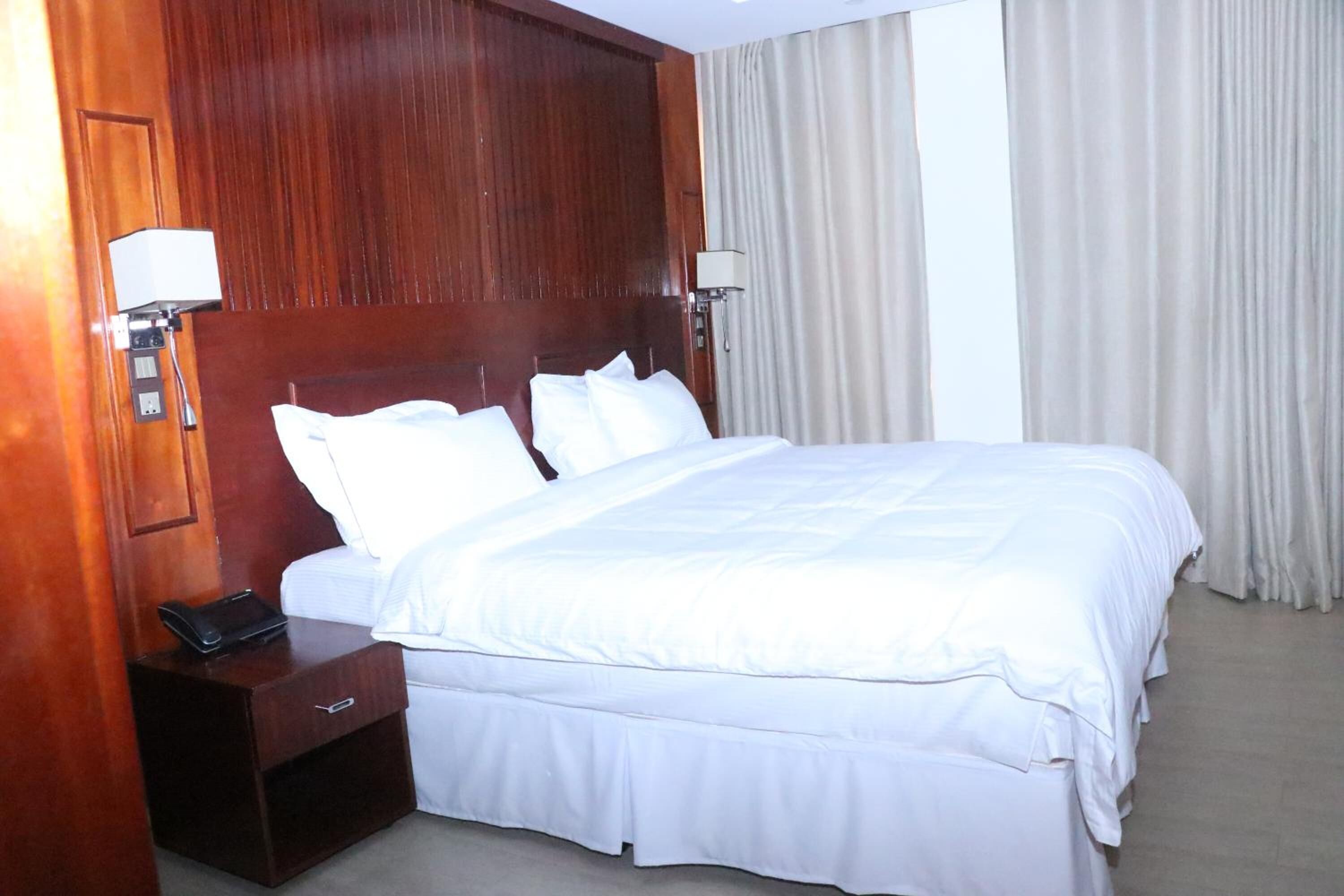 A hotel room with a large bed, wooden headboard, bedside lamps, and a nightstand.