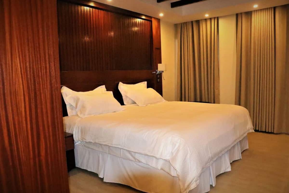 A hotel room with a large bed, wooden headboard, and beige curtains.