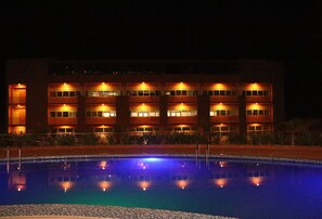 A hotel with a swimming pool, multiple floors, and illuminated windows at night. - Sainte Famille Hotel (Kigali)
