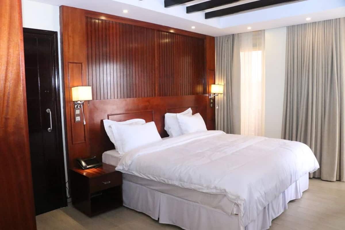 A hotel room with a large bed, wooden headboard, bedside lamps, and a nightstand.