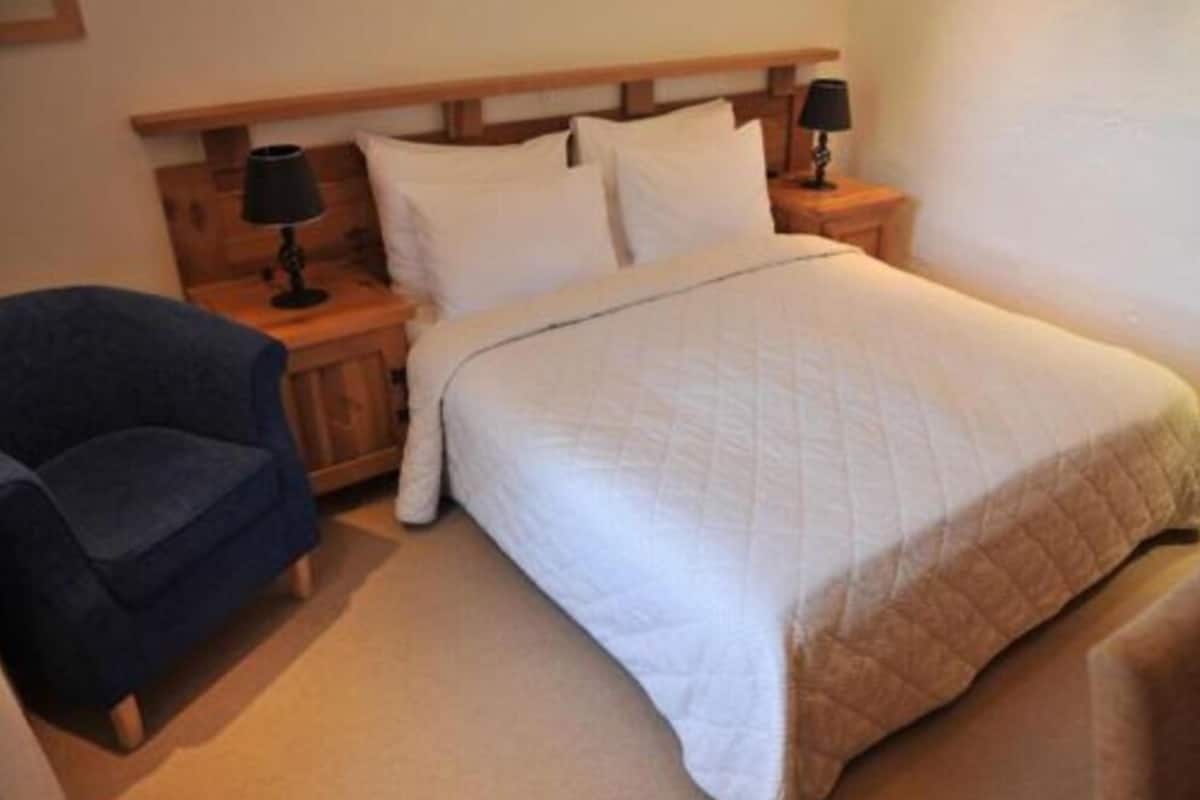A bedroom with a bed, two bedside tables with lamps, a chair, and a wooden headboard.
