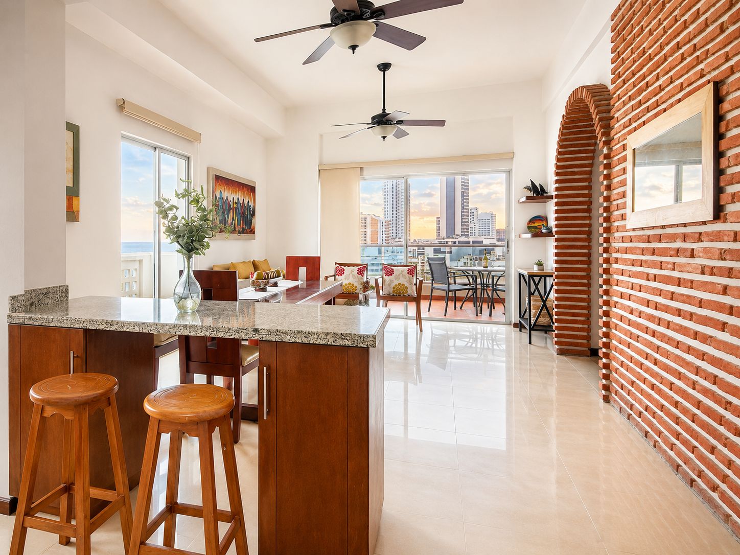 A modern kitchen with a central island, bar stools, and a dining area with a view of the city.