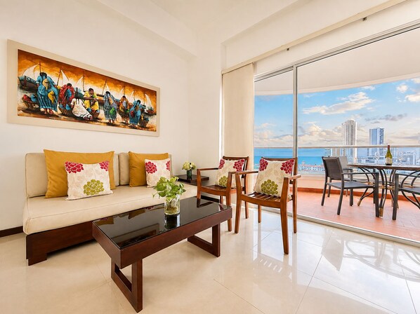 A modern living room with a sofa, coffee table, and chairs, a large painting, and a balcony with a city view.