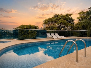 A swimming pool with clear blue water, surrounded by a glass barrier and a metal railing.