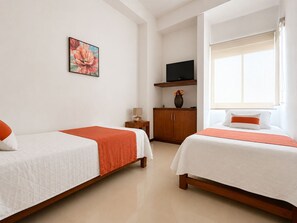 A hotel room with two beds, a television on a shelf, and a window with curtains.