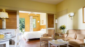 Una habitación de hotel con cama, una zona de estar con sofá y sillas, una mesita pequeña y una mesa de comedor con sillas.
