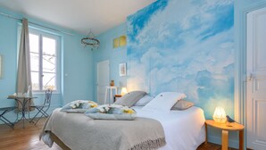 Een slaapkamer met een bed, nachtkastje, stoel, tafel en raam met gordijnen.