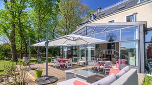 Een terras buiten met een glazen eethoek, rieten meubels en een houten terras.