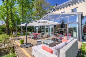 Un patio al aire libre con un área de comedor cubierta con vidrio, muebles de mimbre y una terraza de madera.