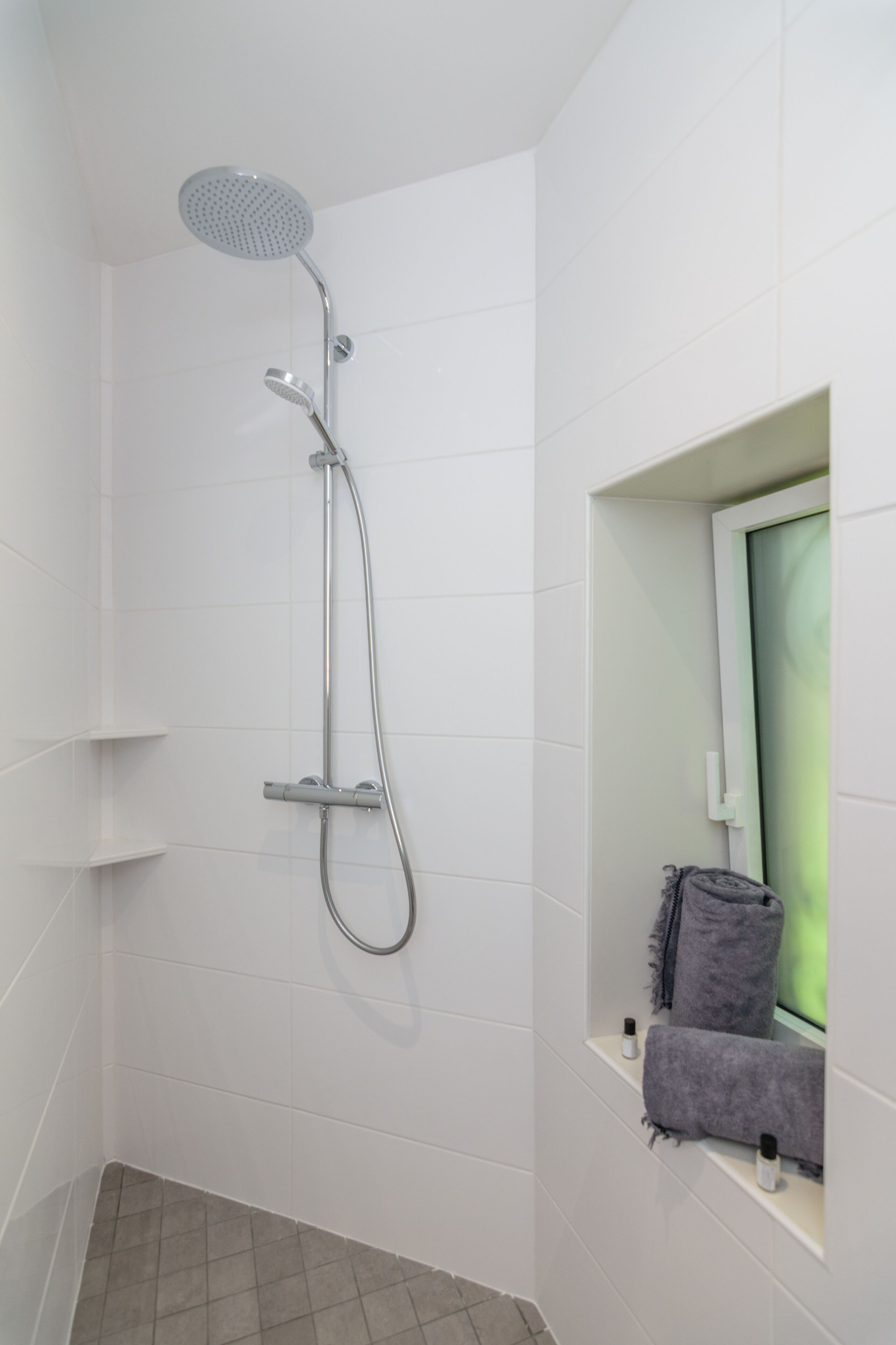 Ein modernes Badezimmer mit Dusche, Handtuchhalter und einer kleinen Ablage für Pflegeprodukte.