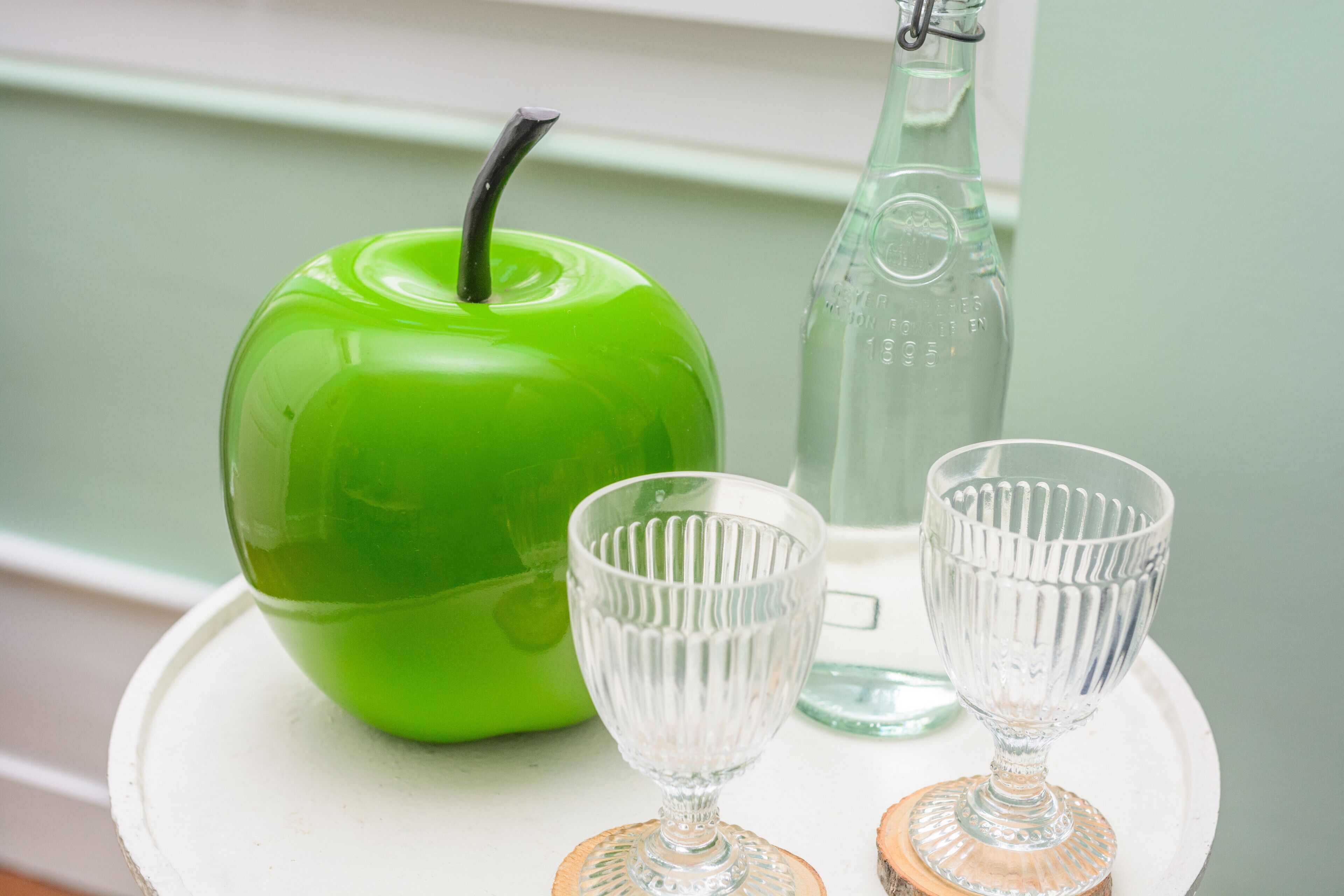Ein grüner Apfel, zwei transparente Gläser und eine Flasche auf einem weißen Tablett.