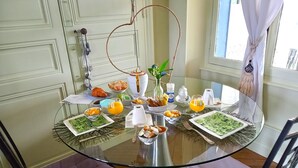 Een ontbijttafel met verschillende soorten eten en drinken, omringd door stoelen en een raam met gordijnen.