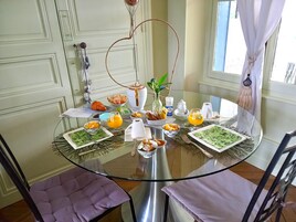 Una mesa de desayuno con diversos alimentos y bebidas, rodeada de sillas y una ventana con cortinas.