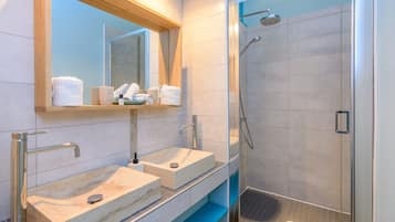 A modern bathroom with a large mirror, two sinks with faucets, and a glass-enclosed shower area.