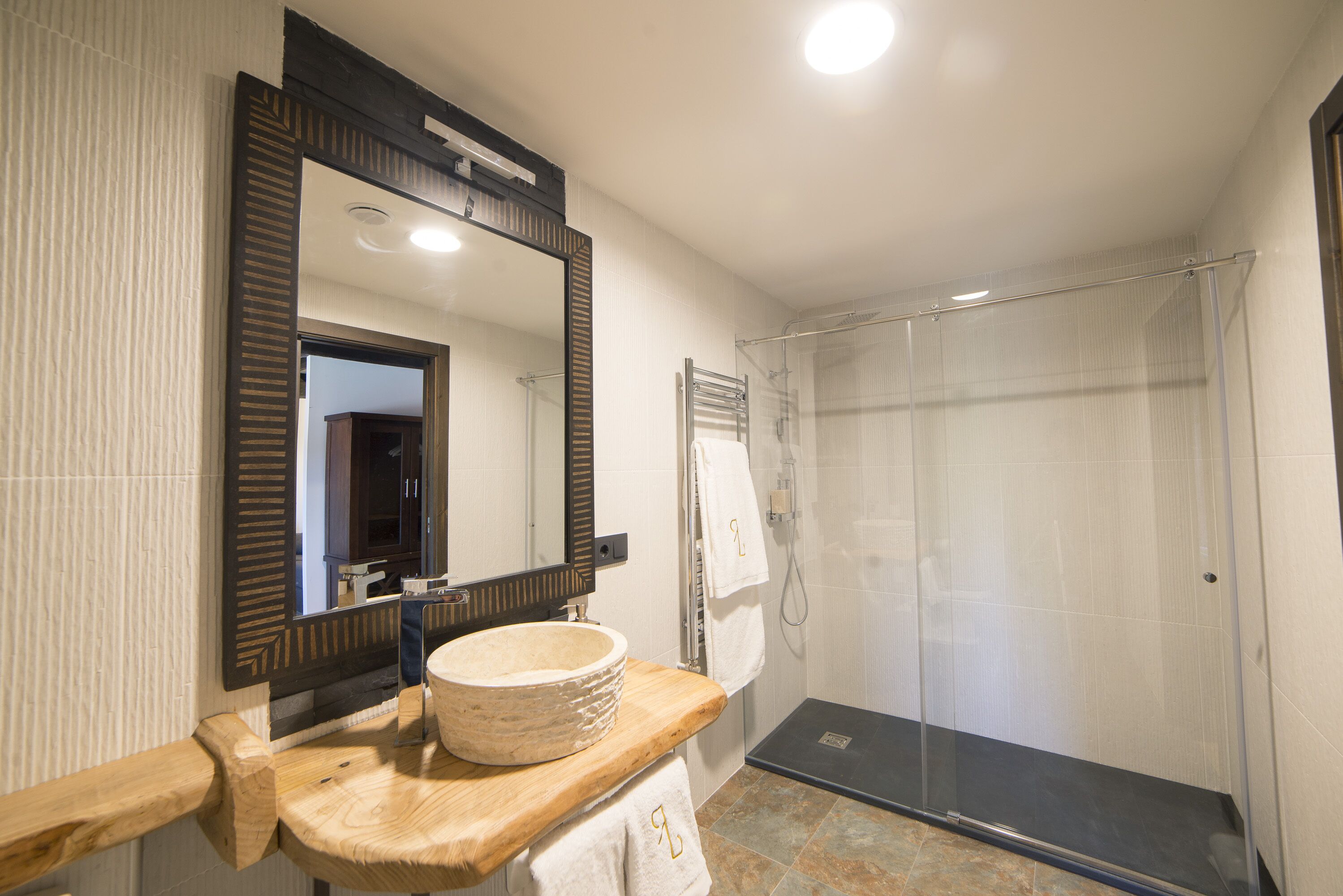 Een badkamer met een houten wastafelmeubel, een grote spiegel, een wastafel en een douche met glazen wanden.