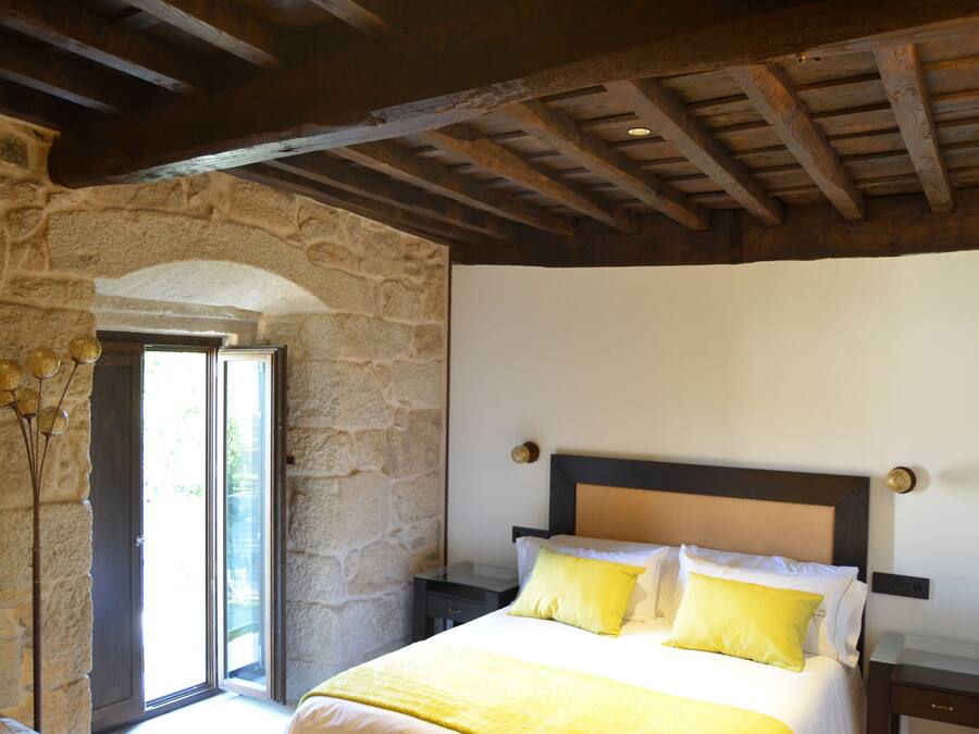 A bedroom with a stone wall, a wooden ceiling, a bed with yellow bedding, and a nightstand.