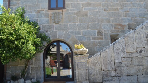 A stone building with a large arched entrance, a window, and a planter with flowers. - Reitoral de Parada (Parada de Sil)