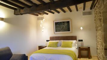 Un dormitorio con cama, mesitas de noche, sofá y pared de piedra.