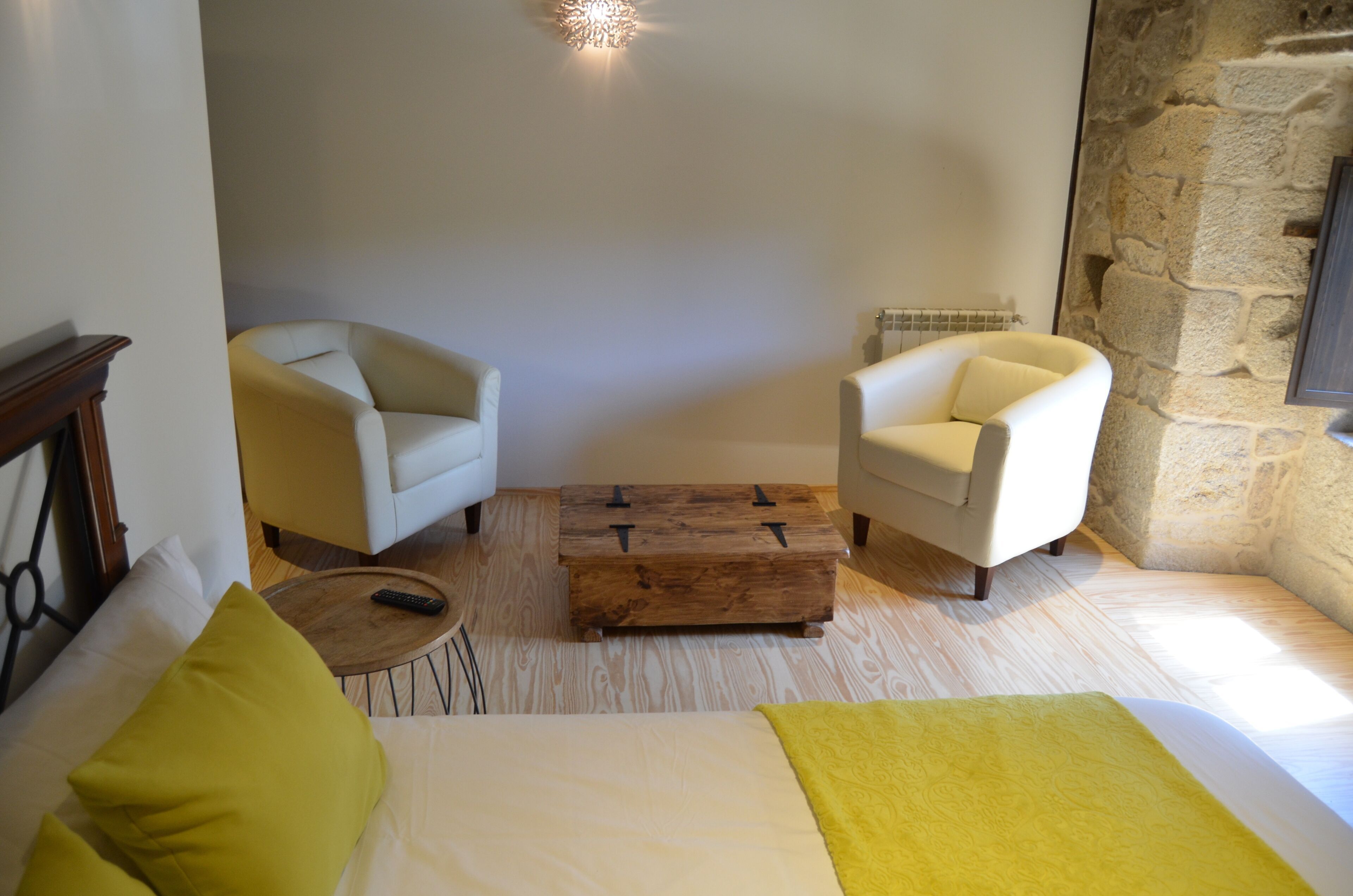 A hotel room with a bed, two armchairs, a wooden coffee table, and a stone wall.