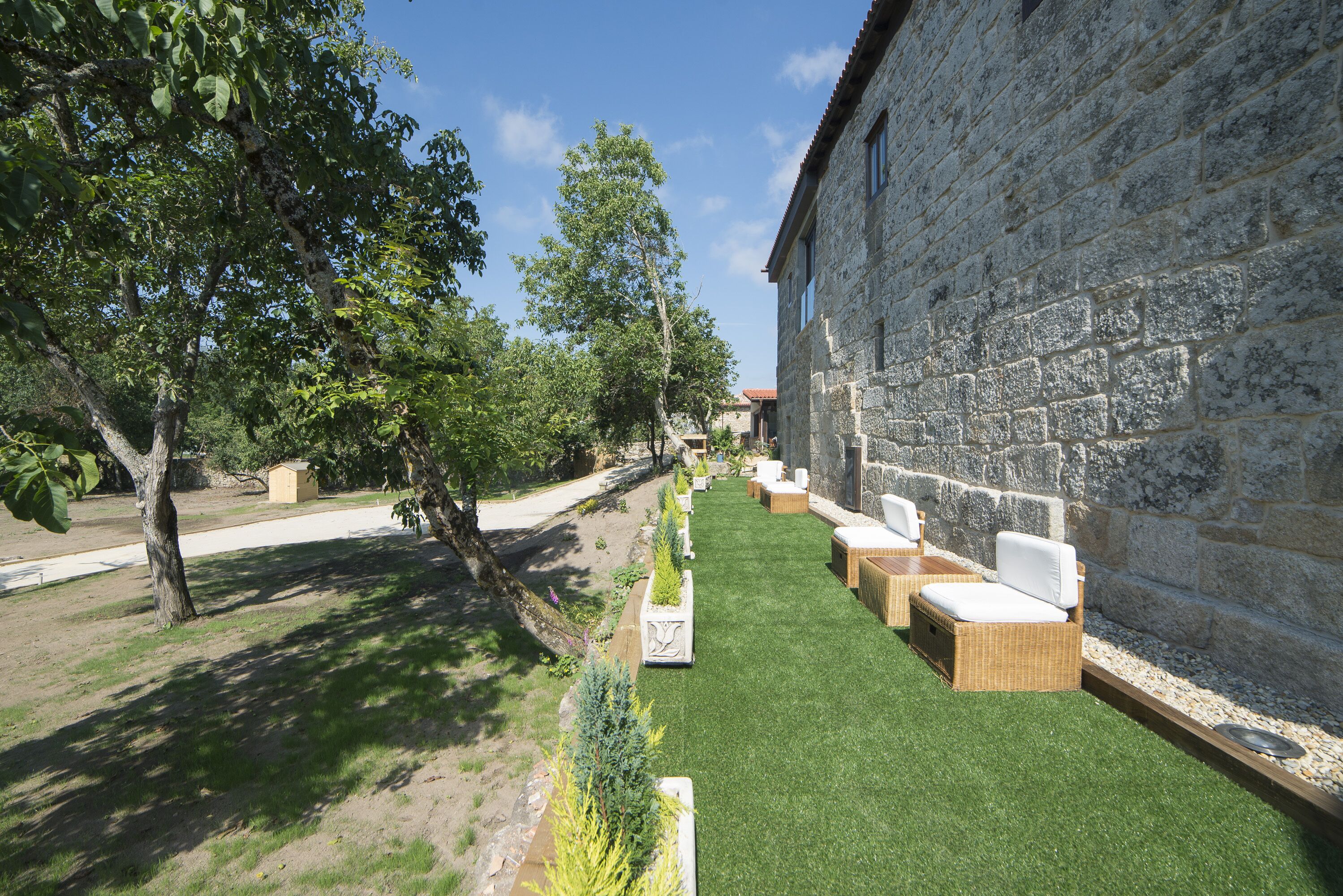 A stone building with a paved pathway leading to a seating area with wicker furniture.
