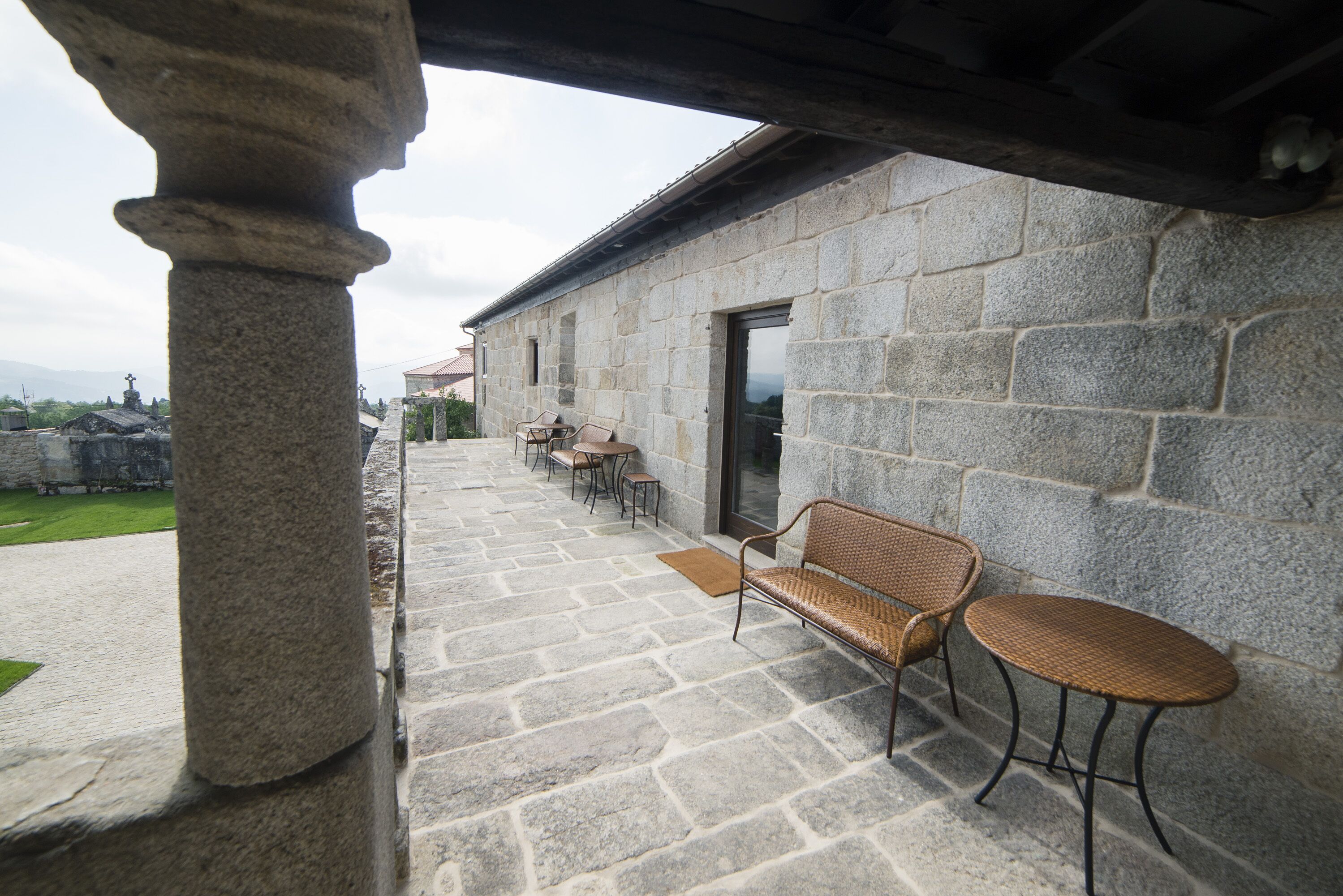 A stone building with a covered patio area, featuring stone flooring, a bench, and two wicker tables.